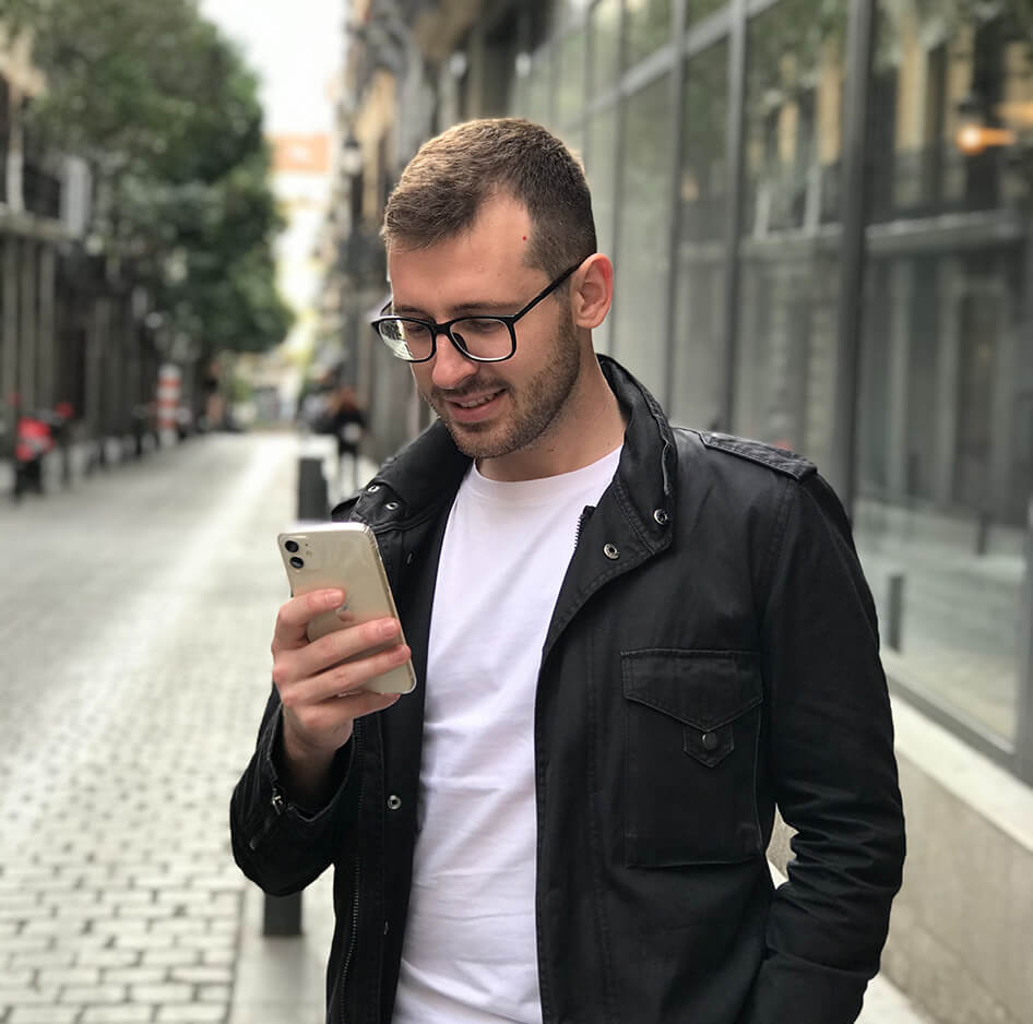 White man with a black jacket and white top holding and looking at his iphone